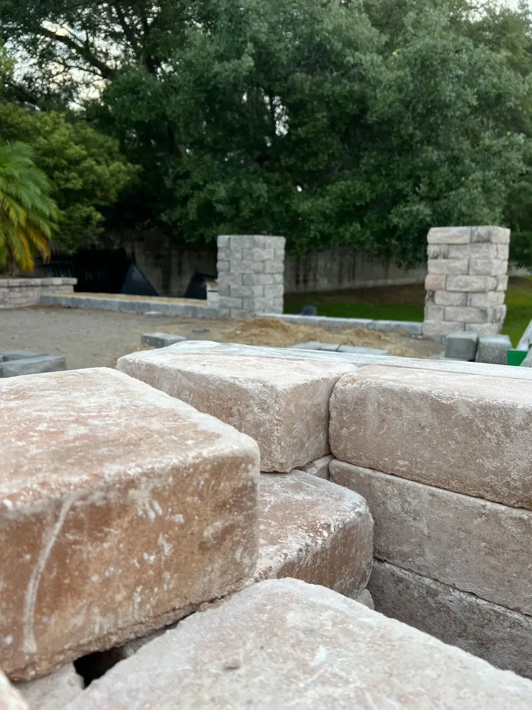 Stacked wall-cap units staged on a job site, with paver columns under construction in the background.