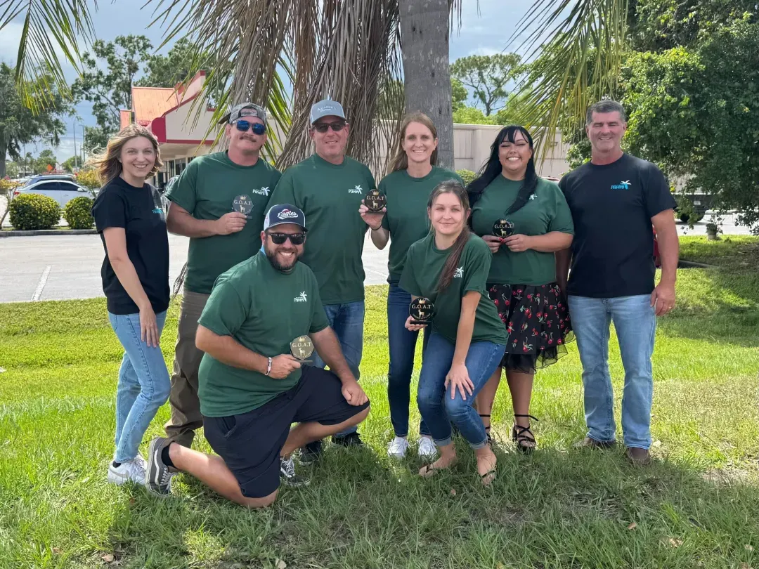 The Alliance Pavers team posing outdoors with G.O.A.T. awards after a company event.