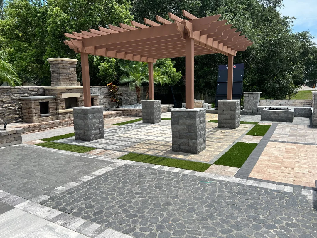 Modern outdoor pergola and paver plaza with a stacked-stone fireplace and fire pit lounge.