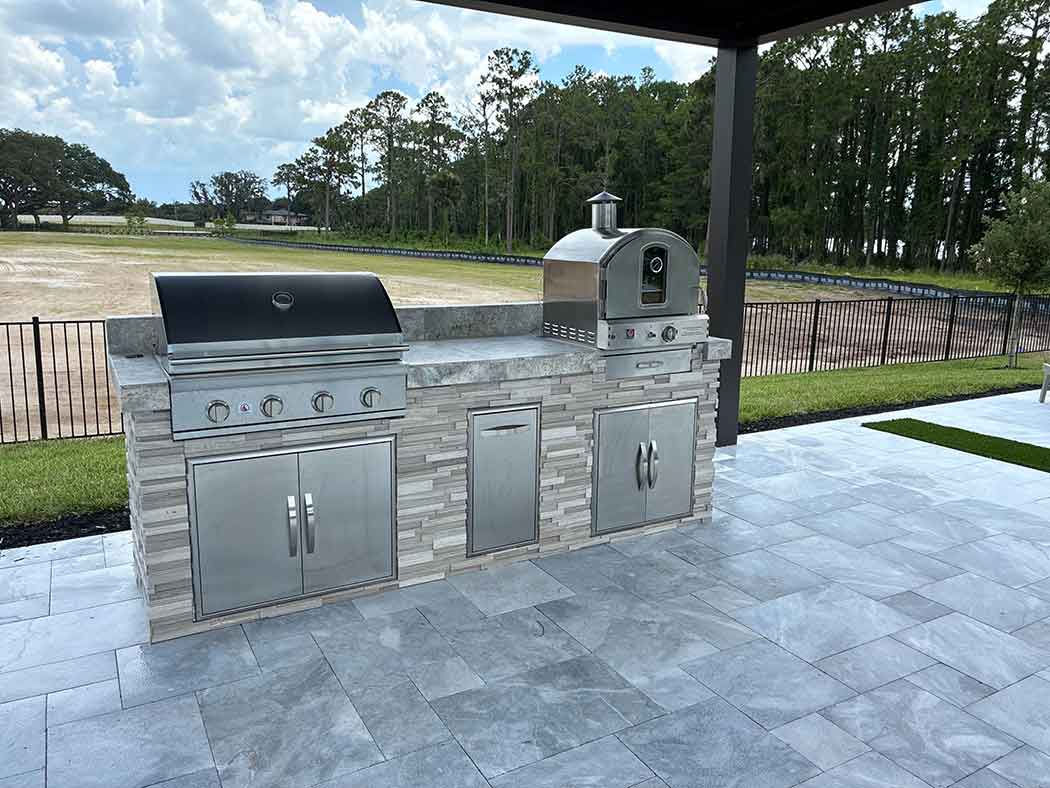 Outdoor kitchen island with grill and pizza oven on paver terrace