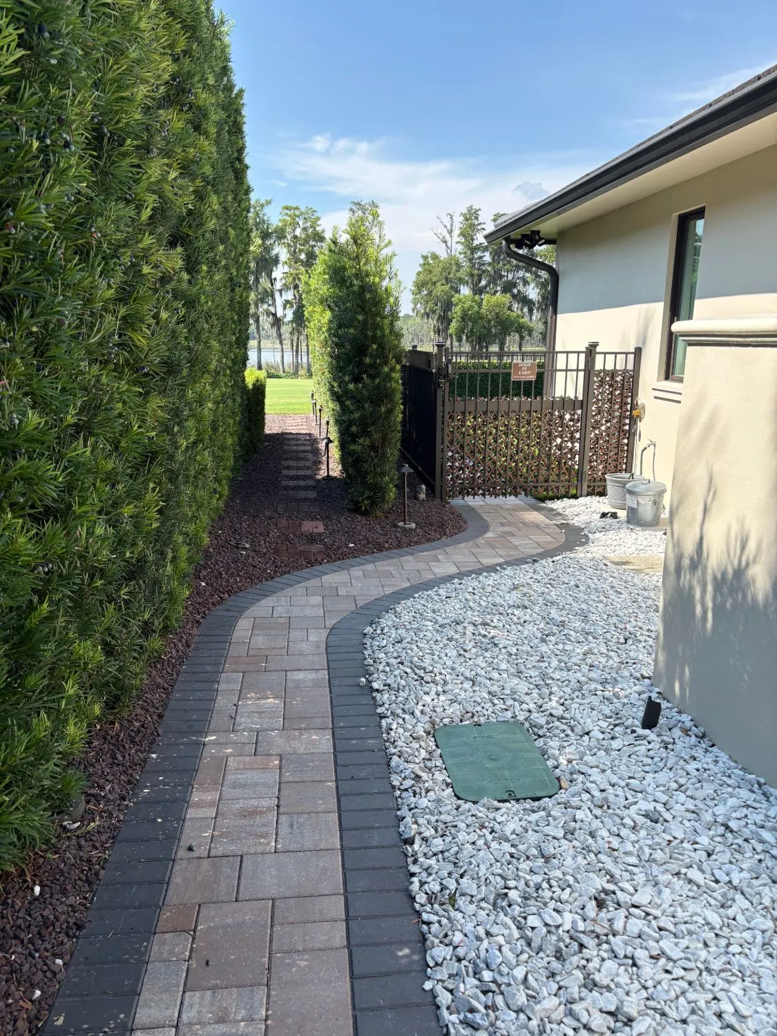 Curving paver garden walkway with dark border and path lighting leading to a gate