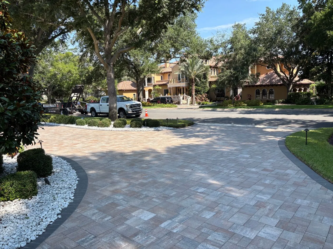 Curving paver motor court with white stone beds and landscape lighting