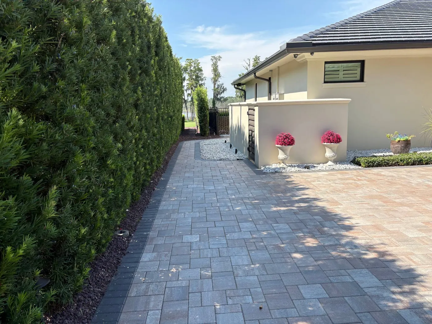 Paver side path with a dark border running along a tall hedge toward the lake