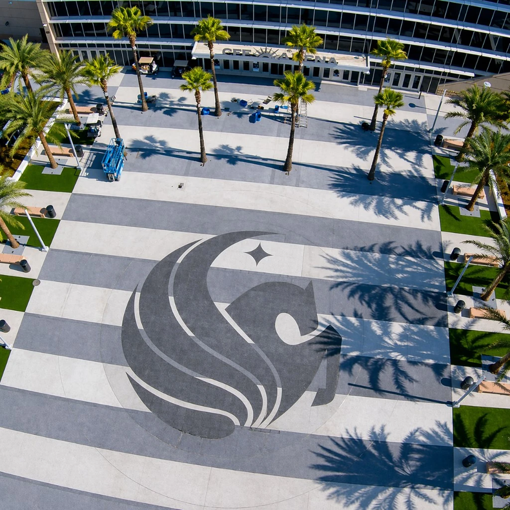 Aerial view of a university arena plaza with a large logo medallion inlaid in contrasting pavers between palm trees
