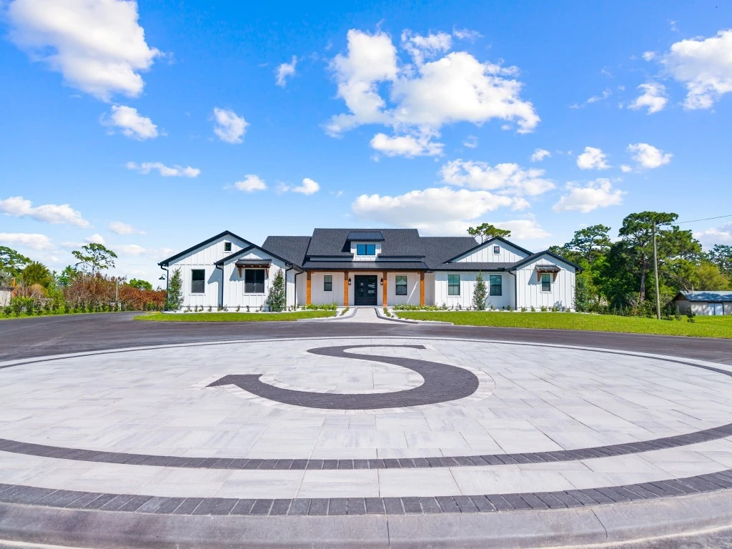 Custom estate circular driveway with an inlaid monogram medallion in front of a modern farmhouse